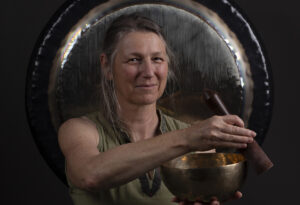 yoga sound image of Heidi playing a brass sing bowl in front of a large brass gong